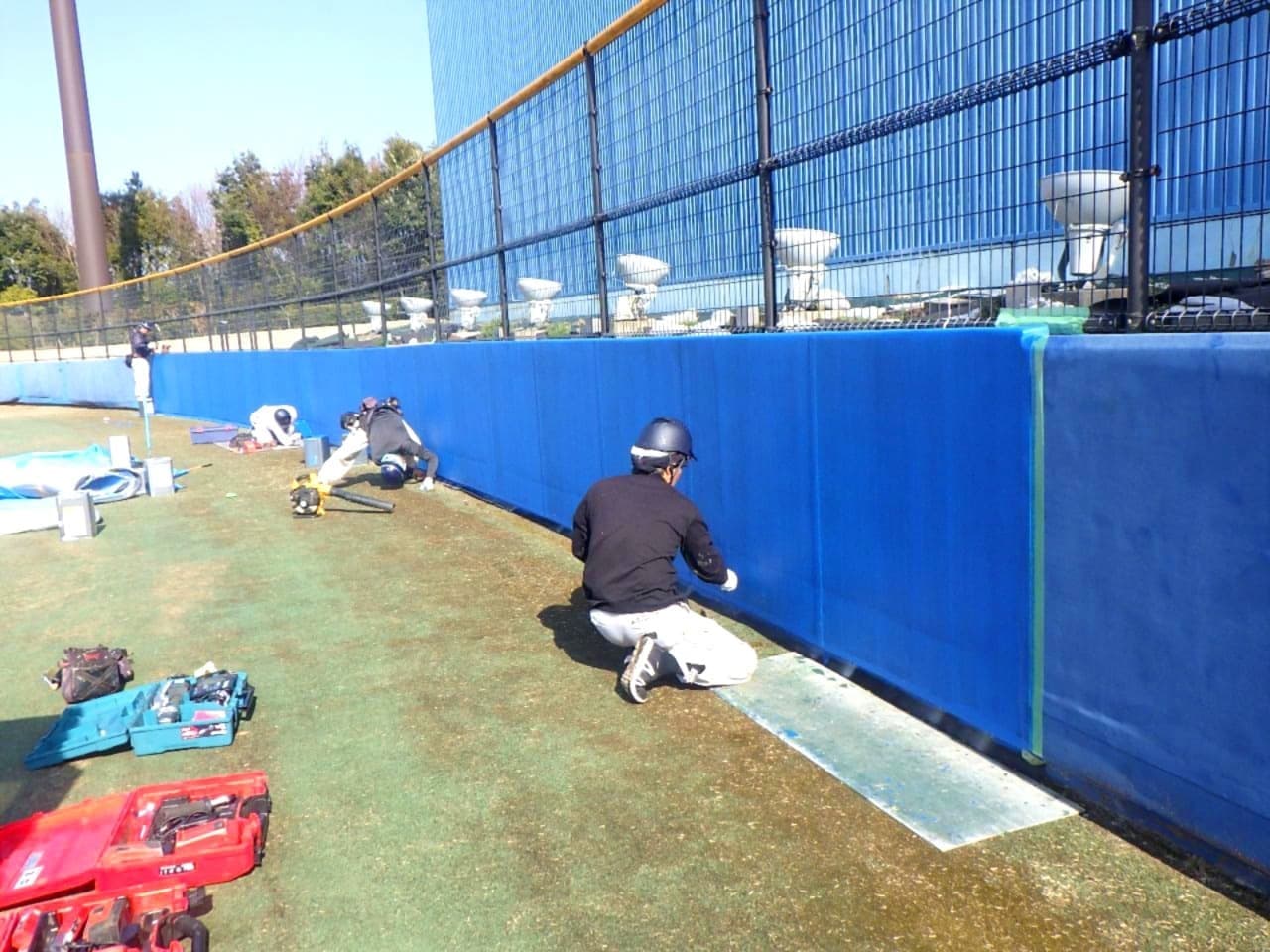 青いフェンスパッド取り付け作業中の作業員の写真